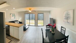 A modern kitchen with a wooden countertop, a dining area with a black table and chairs, and a large sliding glass door leading to a patio.
