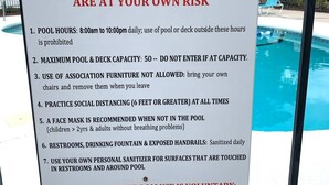 A sign detailing COVID-19 pool rules at Villas on the Green, including pool hours, capacity limits, and safety guidelines.
