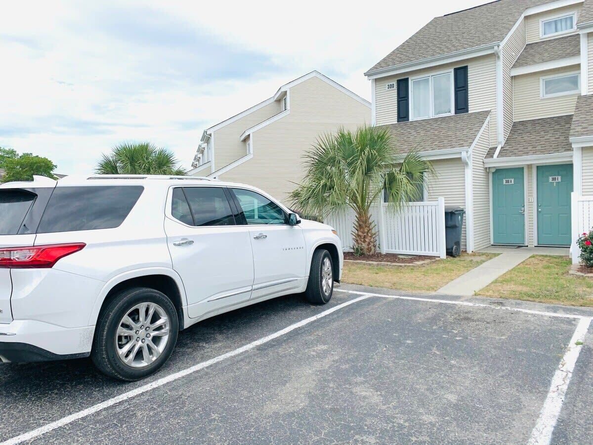 Un SUV blanco estacionado en la entrada de una casa, con otra vivienda al fondo.
