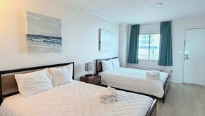 A hotel room with two beds, a painting of the ocean, a window with curtains, and a door. - Carolina Winds #5 beautiful Ocean view condo, pool (Myrtle Beach)