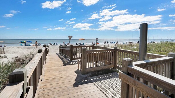 A wooden boardwalk leading to a beach with a clear sky and a few people in the distance. - Carolina Winds #5 beautiful Ocean view condo, pool (Myrtle Beach)