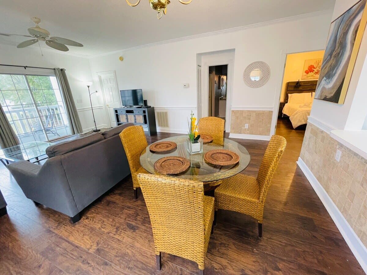 A dining area with a round glass table, wicker chairs, and a grey sofa.