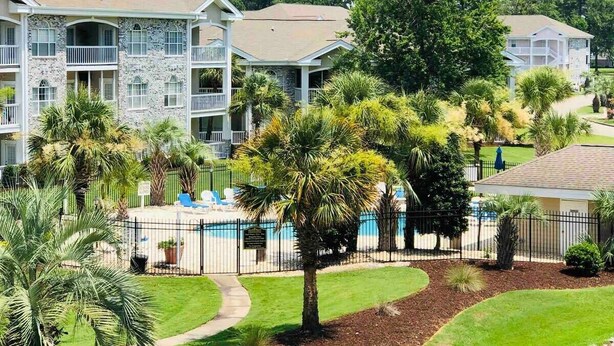 Un edificio a più piani con balconi, una piscina e vegetazione circostante.