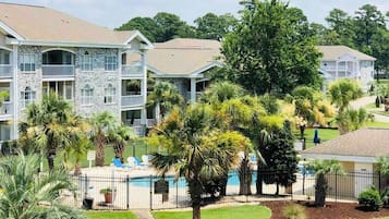 A multi-story building with balconies, a swimming pool, and surrounding greenery.