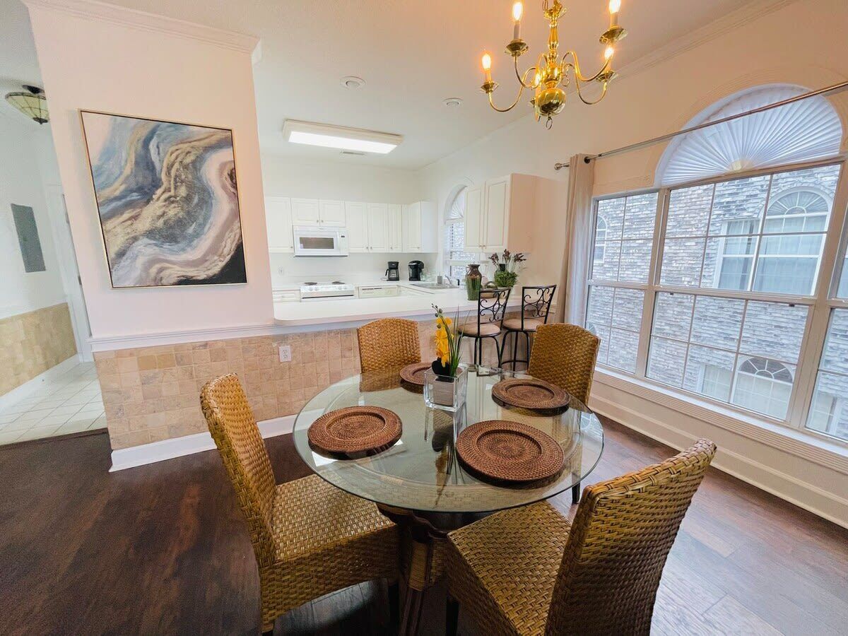 A dining area with a round glass table, wicker chairs, and a chandelier.