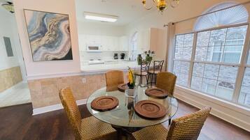 A dining area with a round glass table, wicker chairs, and a chandelier.
