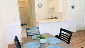 Un coin repas avec une table en bois, quatre chaises noires et des sets de table bleus.