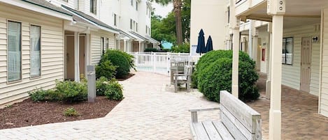 A courtyard with a paved walkway, a wooden bench, and a white picket fence.