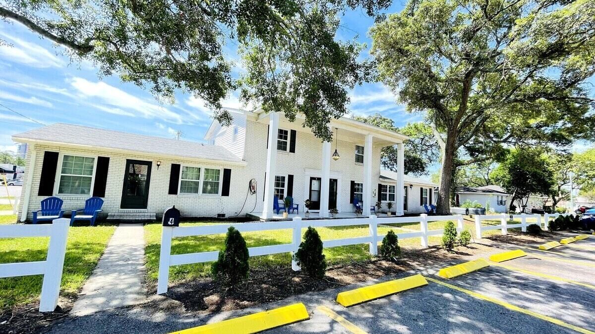 A white building with a porch, blue chairs, and a white fence.