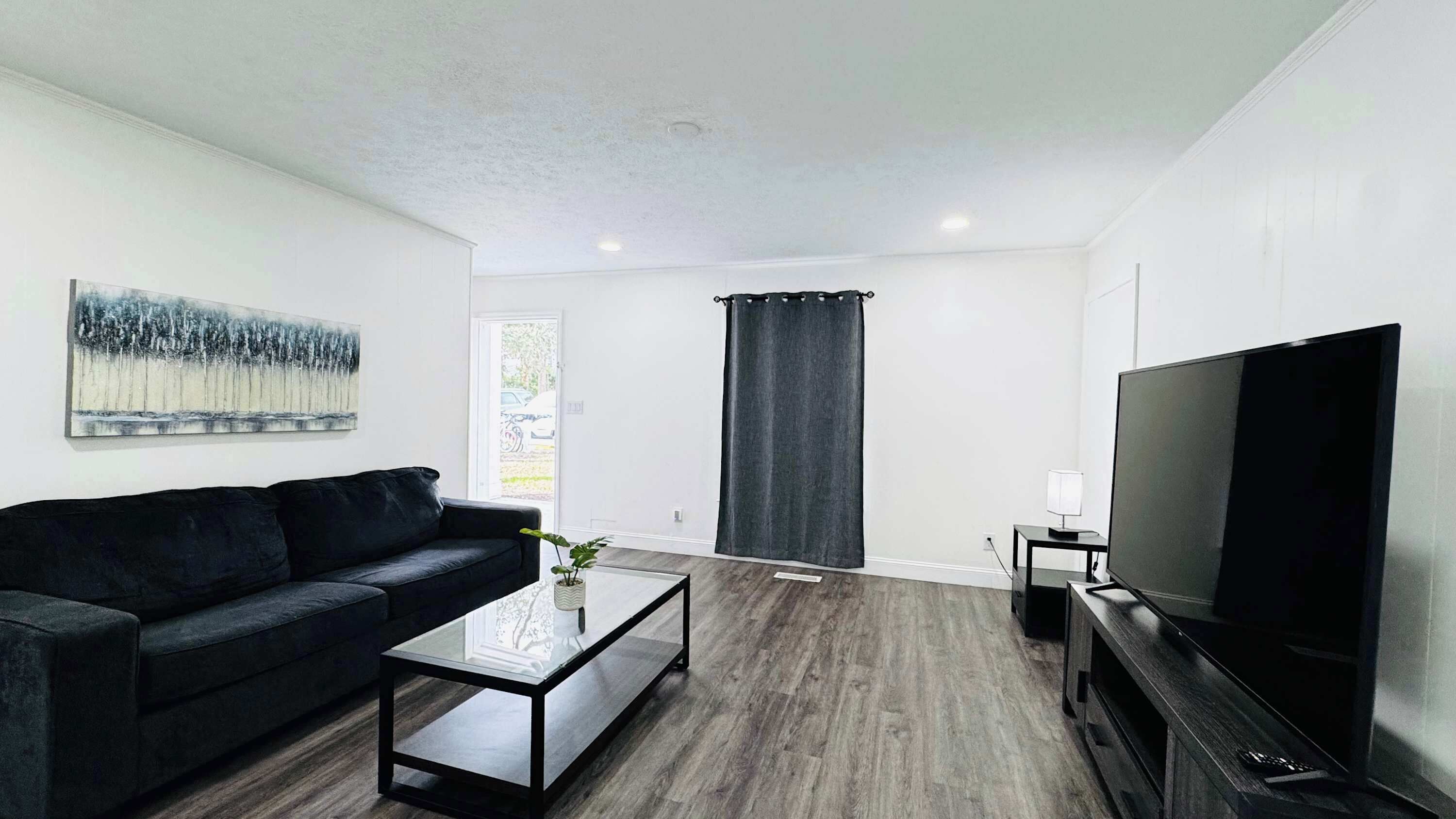 A modern living room with a black leather sofa, a glass coffee table, a flat-screen TV, and a painting on the wall.