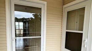 A wooden deck with a glass door entrance, a white door with a window, and a black lantern on the ceiling. - LR1 Bay Tree 1 bedroom condo with pool (Little River)