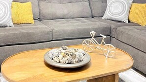 A modern living room with a grey sectional sofa, a wooden coffee table, and a cityscape painting on the wall. - AW3 Stay close to the beach (Myrtle Beach)