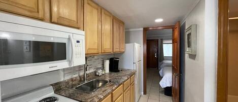 A compact kitchen with wooden cabinets, a white microwave, a stove, and a refrigerator.
