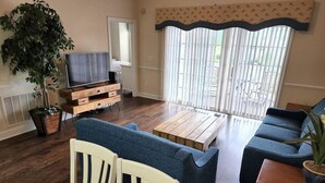 A living room with a television on a wooden stand, a blue sofa, a wooden coffee table, and a potted plant. - The perfect location for your vacation! (Myrtle Beach)
