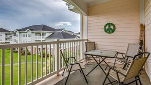 A balcony with a table and chairs, a peace sign decoration, and a view of houses in the background. - The perfect location for your vacation! (Myrtle Beach)