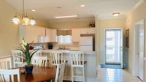 A modern kitchen with white cabinets, a dining table with chairs, and a potted plant. - The perfect location for your vacation! (Myrtle Beach)