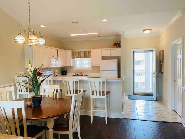 A modern kitchen with white cabinets, a dining table with chairs, and a potted plant. - The perfect location for your vacation! (Myrtle Beach)