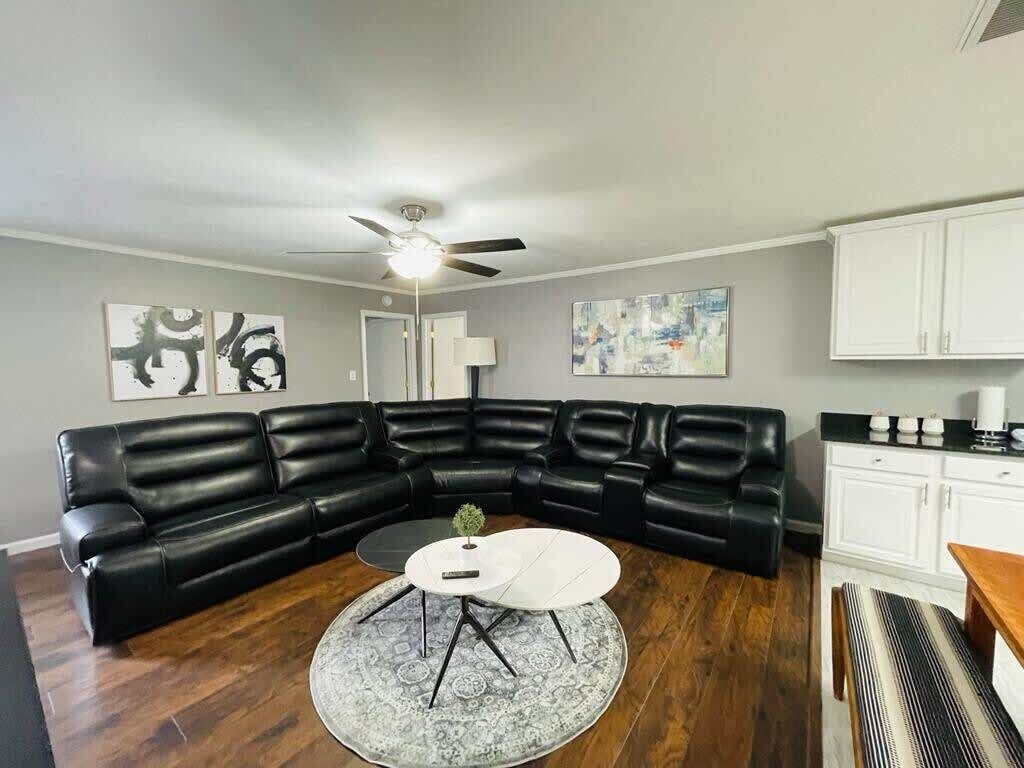 Un salon avec un canapé d’angle en cuir noir, une table basse ronde et un ventilateur de plafond.