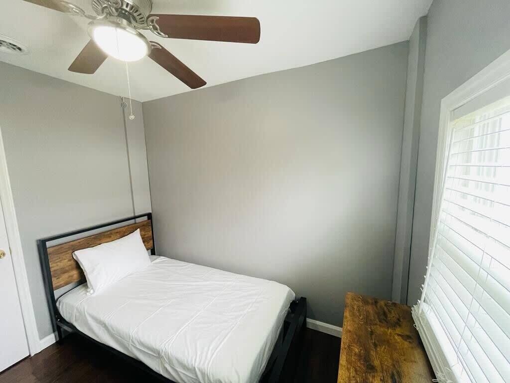A bedroom with a bed, a ceiling fan, and a window with blinds.