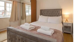 A hotel room with a large bed, a nightstand, a lamp, and a window with curtains. - haven Valley  near the theme park  (Old Windsor)