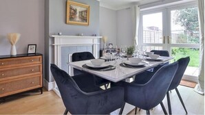 A dining room with a white table set for six, black chairs, a white fireplace, and a large window with a view of greenery. - haven Valley  near the theme park  (Old Windsor)