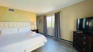 Un dormitorio con una cama grande, un aparador, un televisor y una ventana con cortinas.