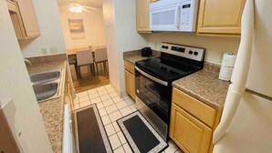 A compact kitchen with a microwave, stove, and sink. There is a dining area with a chair and a table. - Ocean Dunes Villas #17, short walk to the beach (Myrtle Beach)