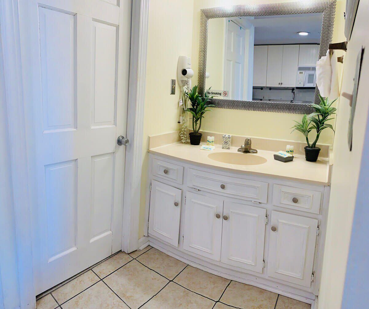 A bathroom with a white vanity, a sink, a mirror with a decorative frame, and two potted plants.
