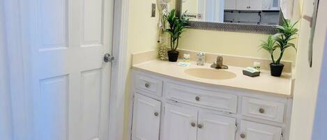 A bathroom with a white vanity, a sink, a mirror with a decorative frame, and two potted plants.