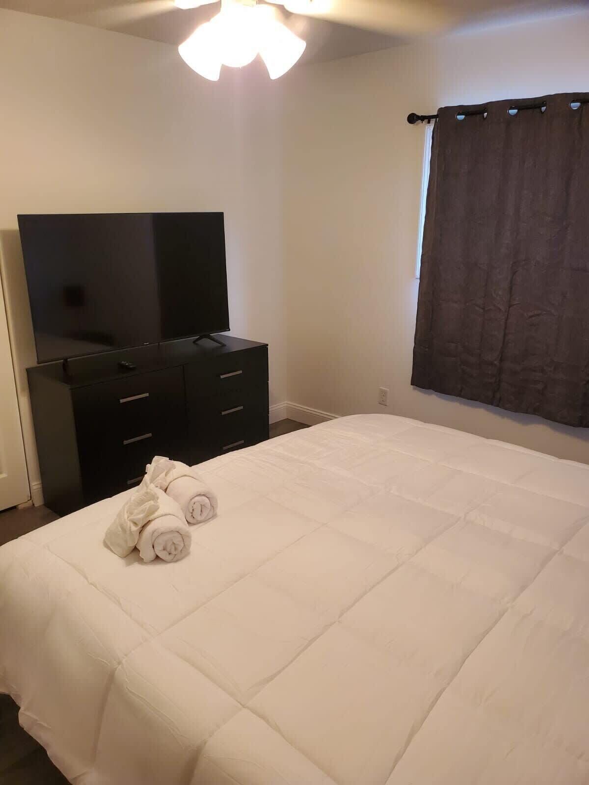 Un dormitorio con cama, televisor en una cómoda y ventana con cortinas.