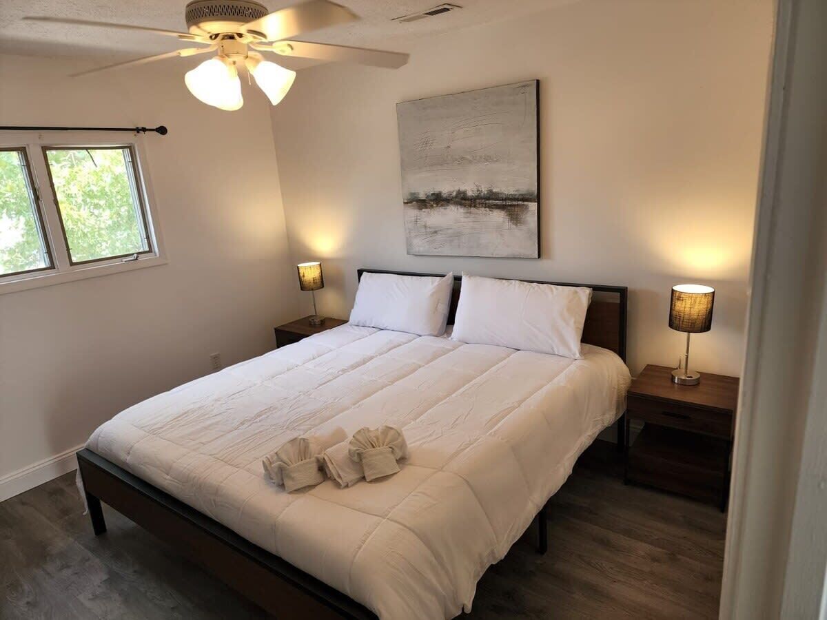 Ein Schlafzimmer mit einem großen Bett, zwei Nachttischlampen, einem Deckenventilator und einem Fenster.