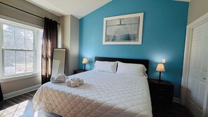 A hotel room with a bed, two bedside tables, a window with curtains, a mirror, and a painting on the wall. - Absolutely Adorable condo in the center of MB (Myrtle Beach)