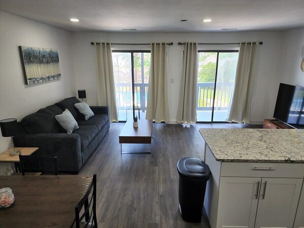 A living room with a sofa, a coffee table, a TV, and a kitchen area with a countertop. - Golf colony amazing condo with pool (Myrtle Beach)