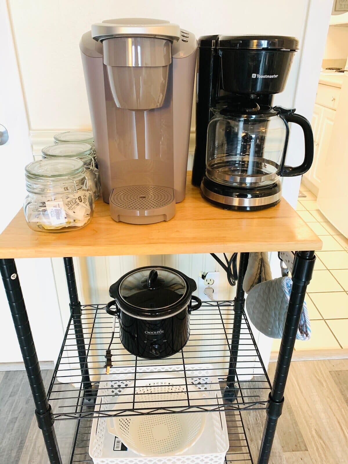 Un piano di lavoro in cucina con una macchina per il caffè, una pentola a cottura lenta e barattoli di tè.
