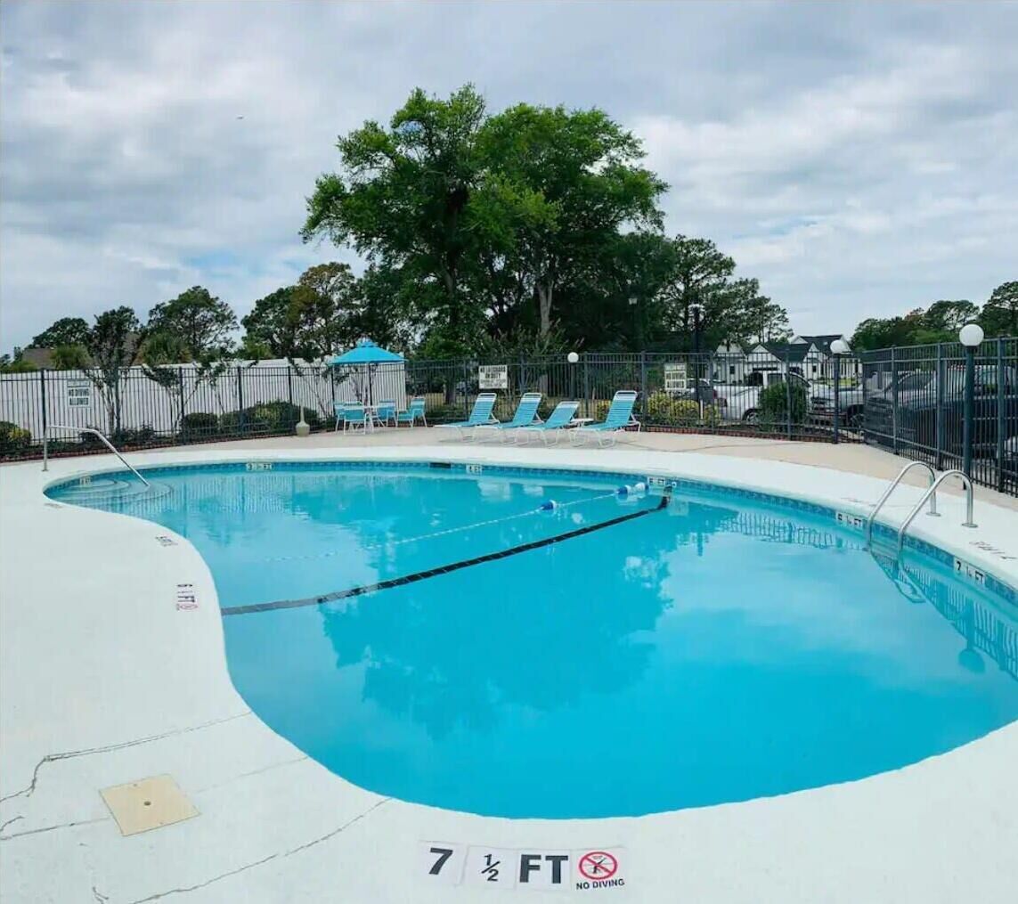 A swimming pool with a 7 1/2 ft depth, surrounded by lounge chairs and a fence.