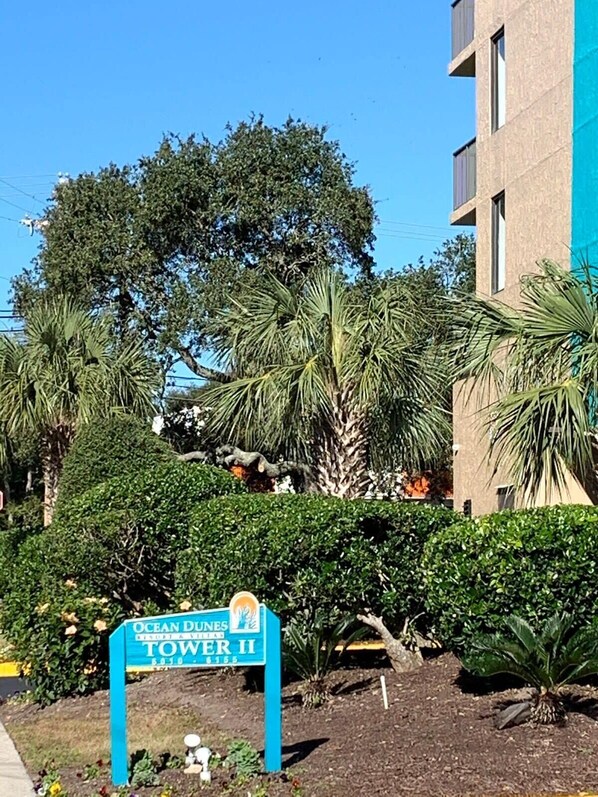 A sign for Ocean Dunes Tower II, surrounded by lush greenery and a modern building. - OD tower II #14, ocean view Fantastic condo + pool (Myrtle Beach)
