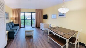 A room with a sofa, a dining table with chairs, a TV mounted on the wall, and a balcony with curtains. - OD Tower I #32, beautiful ocean view condo + pool (Myrtle Beach)