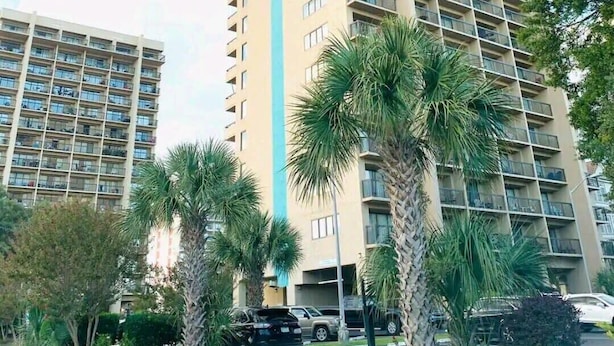 A high-rise hotel with multiple floors, balconies, and a parking area with cars. - OD Tower I #32, beautiful ocean view condo + pool (Myrtle Beach)