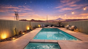 Una piscina rectangular con una cascada, rodeada por un muro bajo con asientos y luces colgantes.
