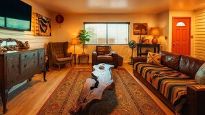 Una sala de estar con una mesa de centro de madera, un sofá de cuero, sillones, un televisor y una ventana con persianas.