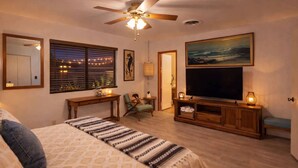 Un dormitorio con cama, escritorio, silla, televisor y ventilador de techo.
