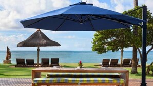 A wooden bench with a plaid cushion, a large blue umbrella, and a thatched umbrella on a wooden deck overlooking a body of water. - Casa 3A Tivoli Ecoresidences - Queen Room 2

 (Açu da Torre)
