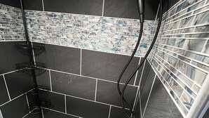 Et bruseområde med sorte fliser, en mosaikflisekant og et brusehoved.