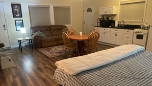 A cozy living room with a sofa, a dining table with chairs, a kitchen area with cabinets and appliances, and a large bed with a checkered blanket.