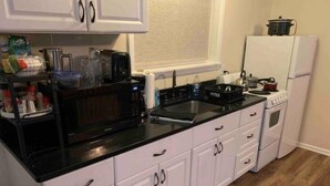 A kitchen with white cabinets, a black countertop, a microwave, a stove, and a refrigerator.