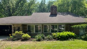 A single-story house with a garage, a chimney, and a front yard with various plants.