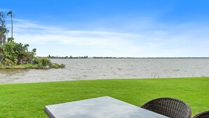 A grassy area with a table and chairs facing a body of water, with trees and a distant shoreline. - Yarrawonga Lakeside Apartment 41 (Mulwala)