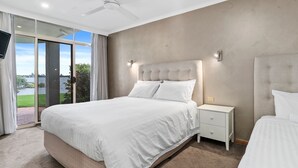 A modern bedroom with a large bed, a nightstand, a ceiling fan, and a view of a body of water through a sliding glass door. - Yarrawonga Lakeside Apartment 41 (Mulwala)