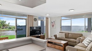 A modern living room with a TV, sofa, and large windows overlooking a body of water. - Yarrawonga Lakeside Apartment 41 (Mulwala)