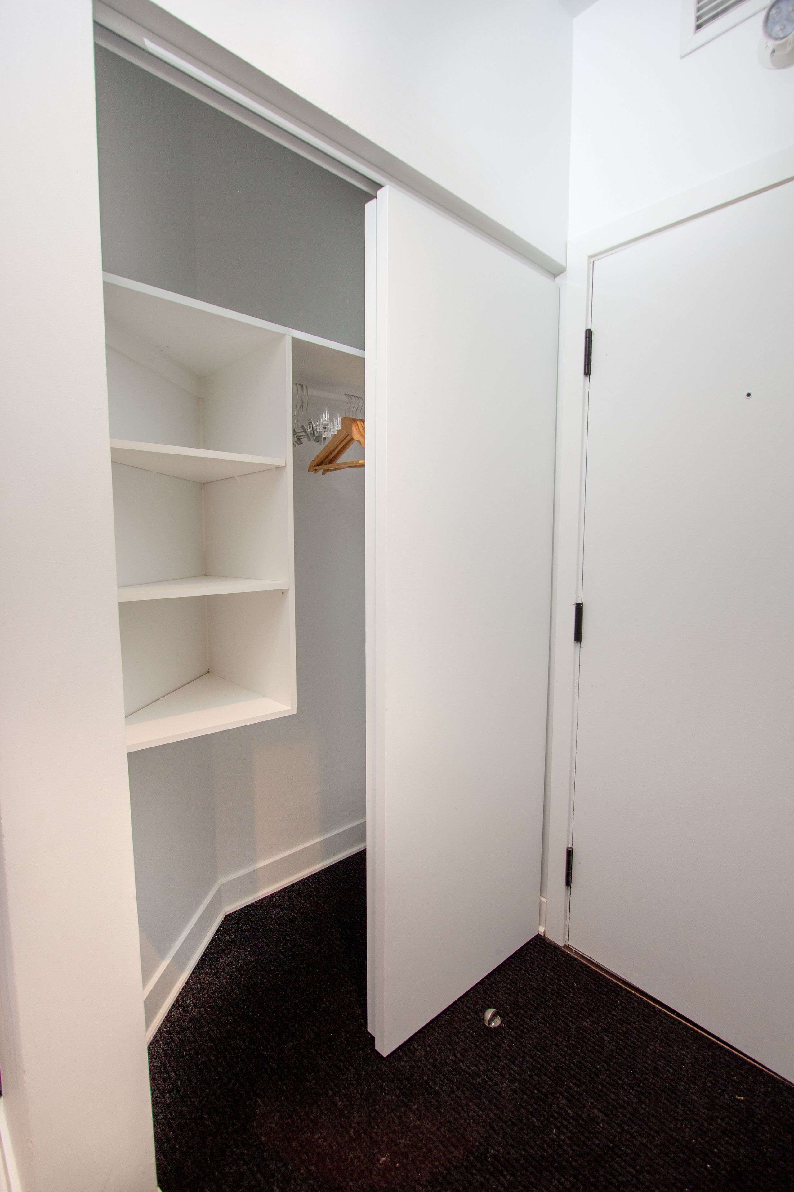 Een witte kast met open deuren, waar planken en een kledingroede zichtbaar zijn.